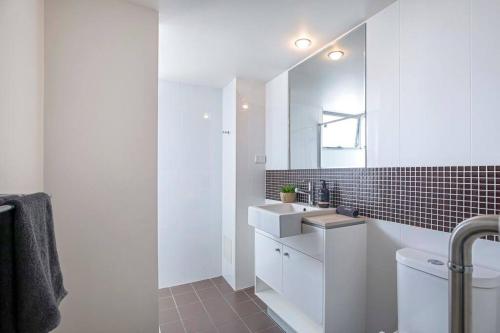 Baño blanco con lavabo y espejo en Stadium Vue, 3Bd,Riverview Pool, 300m to S/Stadium en Brisbane