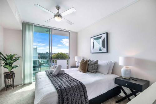 Dormitorio blanco con cama y ventana grande en Stadium Vue, 3Bd,Riverview Pool, 300m to S/Stadium en Brisbane