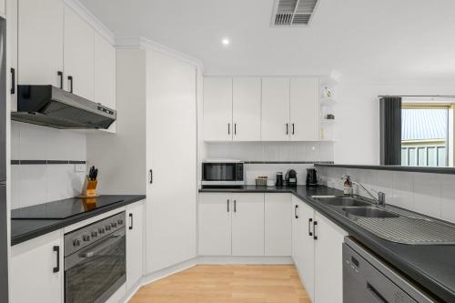 a kitchen with white cabinets and black counter tops at Beltana - Aldinga Beach - C21 SouthCoast Holidays in Aldinga Beach