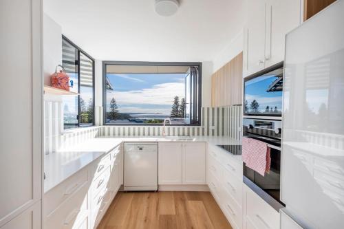 a kitchen with white cabinets and a large window at Namanula 7 - oceanstays in Yamba