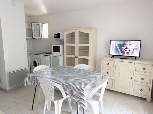 une cuisine avec une table et des chaises blanches ainsi qu'une télévision dans l'établissement Maison proche plage, commerces, 6 pers., terrasse, parking privé, option Internet, animaux non admis - FR-1-387-196, à Marseillan