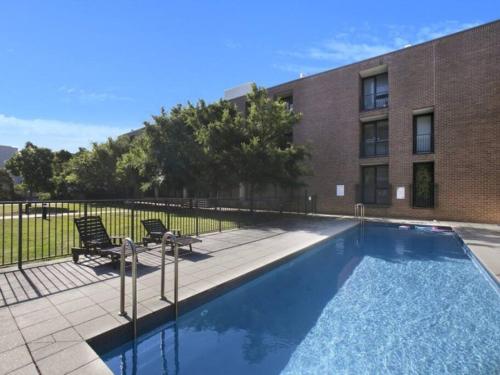 雪梨的住宿－Stylish parkside retreat，一座带两把椅子的游泳池位于大楼旁