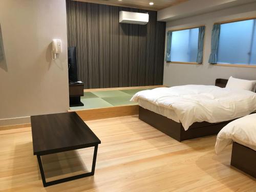 a bedroom with two beds and a table and a television at Tabist Hotel Chouseikaku in Yatsushiro