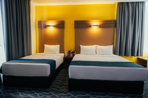 two beds in a hotel room with yellow walls at Hotel Sentral Kuantan @ Riverview City Centre in Kuantan