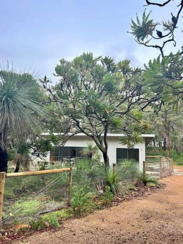a white house with a fence and some trees at Rosella - Bushland Hideaway in Yallingup