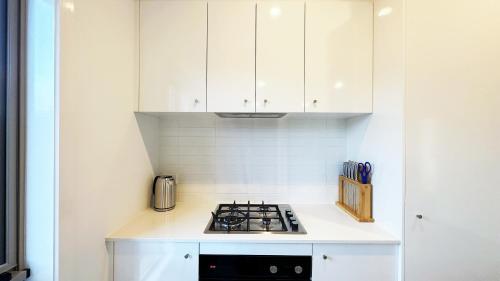 a white kitchen with a stove and white cabinets at The Grove Home by GoodLive in Tarneit