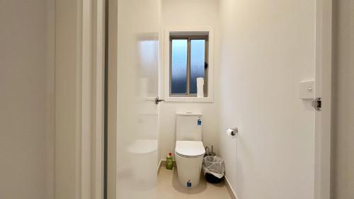a white bathroom with a toilet and a window at The Grove Home by GoodLive in Tarneit