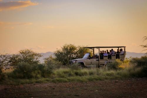 Okapuka Safari Lodge في ويندهوك: مجموعة من الناس يركبون في الجزء الخلفي من شاحنة