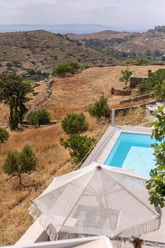 a swimming pool with an umbrella next to a field at Kea Villa Thea- Villa Ilios in Vourkarion