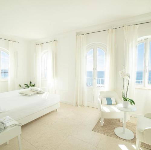 a white bedroom with a bed and a chair at Relais La Ghinghetta in Portoscuso