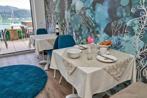 a dining room with tables and blue chairs and a wall at Appartements am See in Maria Wörth