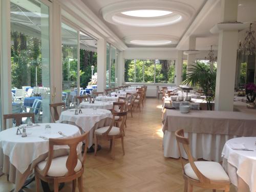 a restaurant with white tables and chairs and windows at Hotel Royal in Stresa
