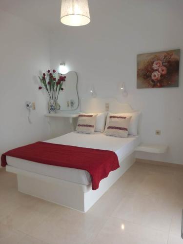 a white bedroom with a white bed with a red blanket at Klimataria Studios in Agios Prokopios