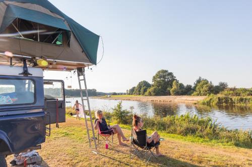 two women sitting in chairs next to a river at Chalets De Roos in Beerze