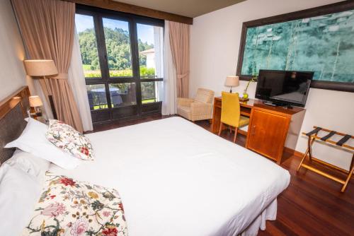 TorazoにあるHosteria de Torazo Nature Hotel & Spaのベッド、デスク、テレビが備わるホテルルームです。