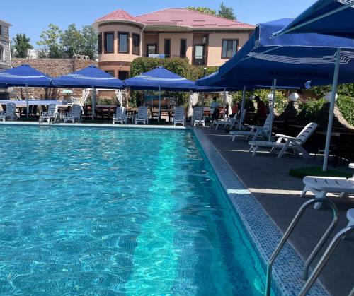 a swimming pool with blue umbrellas and tables and chairs at Вилла Эдем in Shymkent