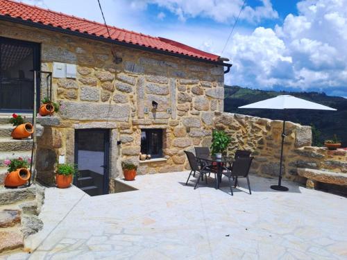a stone house with a table and chairs and an umbrella at Casa da Carrasqueira in Soajo