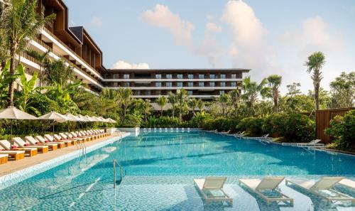 ein Pool mit Stühlen und ein Hotel im Hintergrund in der Unterkunft The Taikang Sanya, a Tribute Portfolio Resort in Sanya