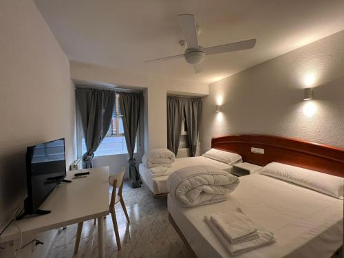 a hotel room with two beds and a desk and a television at Hostal la Embajada in Talavera de la Reina