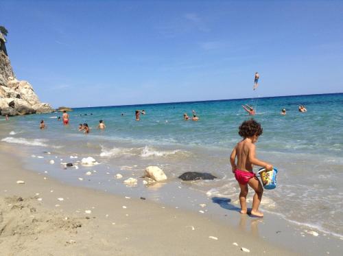 a young boy standing on a beach with people in the water at B&B Luce Viola in Dorgali