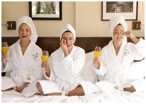 Kerpė Hotel & SPA في بالانغا: ثلاث نساء يجلسن على سرير مع كؤوس من النبيذ