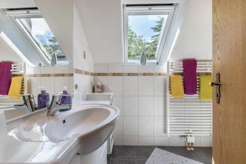 a white bathroom with a sink and two windows at Ferienwohnung Haus am Wald in Meßstetten