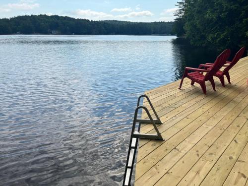 two red chairs sitting on a dock on a lake at Camp Lake Bear in South Colton