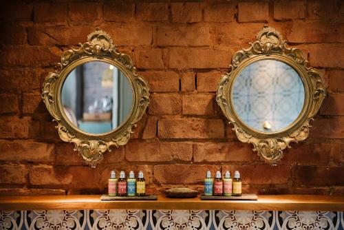 two mirrors on a brick wall with bottles on a shelf at Le Petit Chateau & William de Percy in Otterburn