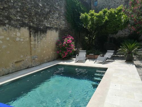 a swimming pool with two chairs and flowers at Gîte de l ancienne Poste in Bourdic
