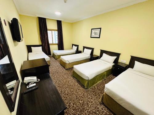 a hotel room with three beds and a television at Nada Al Majd Hotel in Makkah