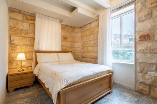 1 dormitorio con cama y pared de piedra en Via Maria Boutique Suites In The Middle Of The city, en Haifa
