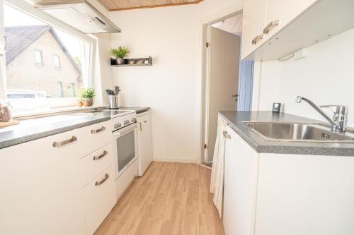 uma cozinha com armários brancos, um lavatório e uma janela em Parkvejens feriebolig em Bindslev