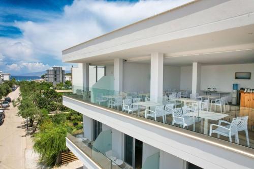 uma varanda com cadeiras brancas e mesas num edifício em Otto Hotel em Ksamil