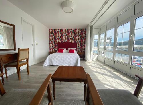 a bedroom with a bed and a desk and windows at Pensión Residencia J. Lago in Muros