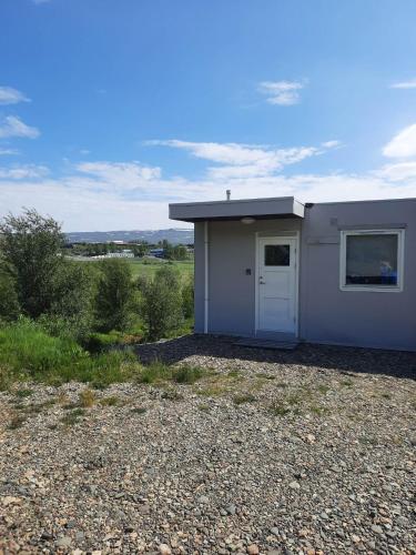 un petit bâtiment blanc avec une porte dans un champ dans l'établissement Vinland Apartment 2, à Egilsstaðir