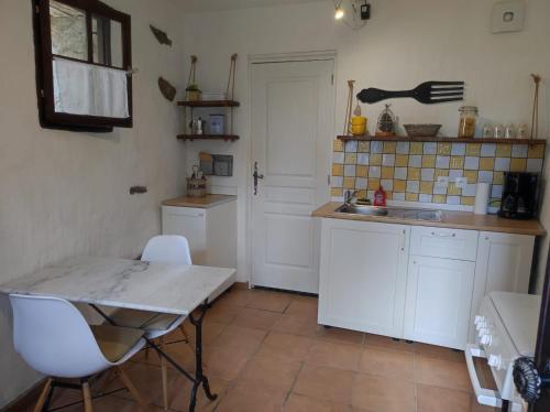 cocina con armarios blancos, mesa y fregadero en Sole e Ventu 30qm, en San-Giovanni-di-Moriani