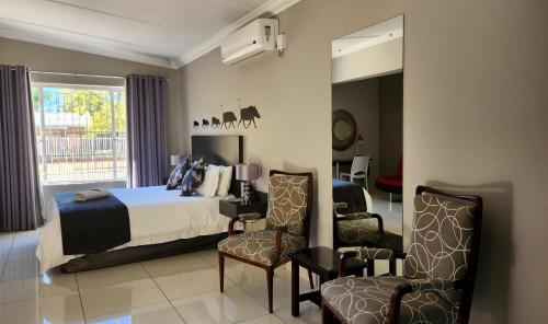 Green Kalahari Guesthouse في آبنغتون: غرفة نوم بسرير وكرسيين ومرآة