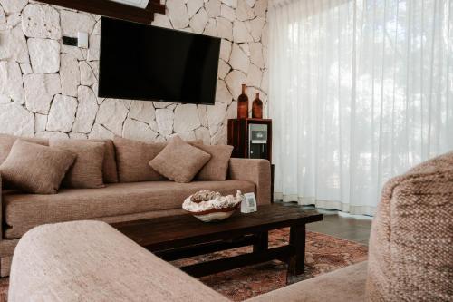 a living room with a couch and a tv on a stone wall at Kaaba Luum Jungle Villas in Chemuyil