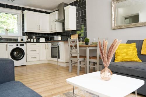 a kitchen and living room with white cabinets and a table at Rotherwood Apartment in Glasgow