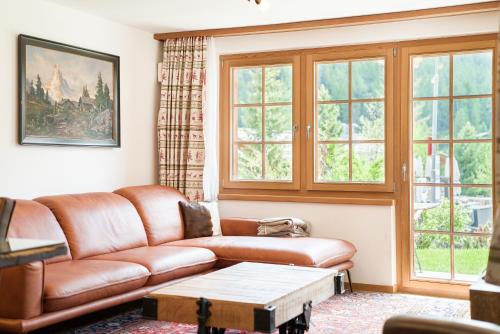 a living room with a brown leather couch and windows at Chalet Ulysse in Zermatt