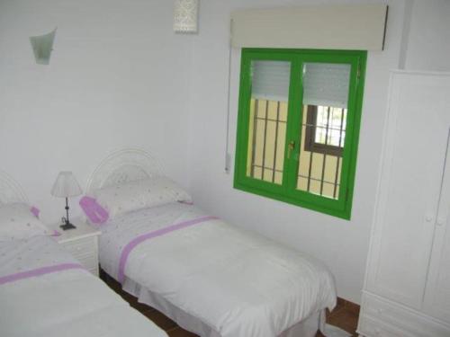 two beds in a room with a green window at La Fuente, apartment in the Moorish quarter. in Frigiliana