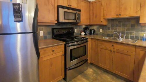 a kitchen with a stainless steel refrigerator and wooden cabinets at Settlers Crossing #29 By Bear Country in Sun Peaks