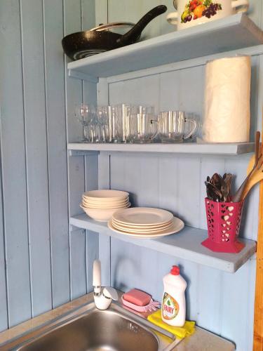 a kitchen sink with plates and dishes on shelves at Апарт-отель "У речки" in Kuchkisabano