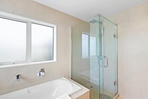 een badkamer met een bad en een glazen douche bij Spacious Modern 3BR Home - WiFi Netflix - Office in Karaka