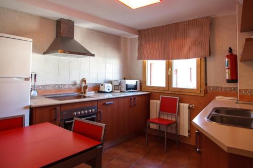 une cuisine avec des placards en bois, une table rouge et des chaises dans l'établissement Apartamentos turísticos el gamo, à Tragacete