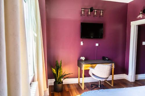 Habitación púrpura con escritorio y TV en la pared. en Manoir Becancourt Hotel, en Bécancour
