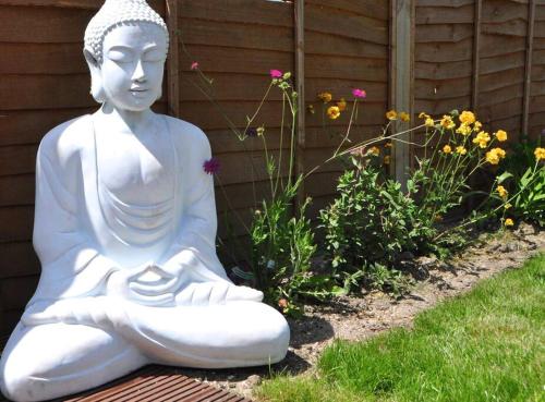 a white statue sitting in the grass near some flowers at Luxury house in The New Forest in Sway