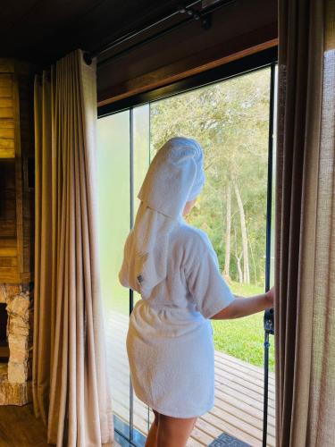 a woman in a white dress looking out of a window at Sunset Serrano Chalés in Urubici