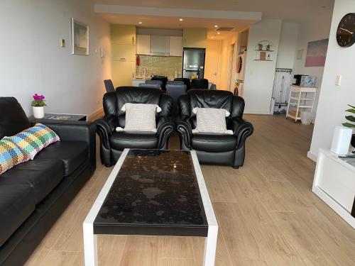 a living room with black leather couches and a table at Glenelg resort style beachside apartment in Glenelg