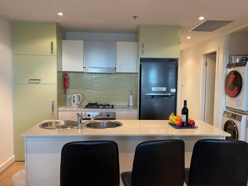 Glenelg resort style beachside apartment في غلينلغ: مطبخ مع حوض وكاونتر مع كراسي